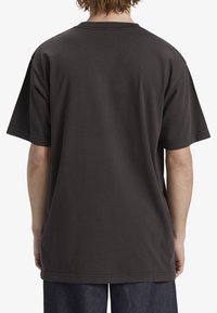 T-shirt de algodão cinza escuro com um corte descontraído, mangas curtas e bainha reta. Detalhes de costura nos ombros. Vista traseira lisa.