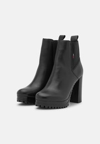 Czarne skórzane botki za kostkę z wysokim słupkowym obcasem, okrągłym noskiem, elastycznymi panelami bocznymi i teksturowaną podeszwą zapewniającą przyczepność.