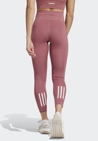 Hoch taillierte, rosa Leggings aus einem glatten, dehnbaren Material mit drei vertikalen weißen Streifen an den Unterbeinen.