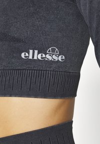 Dark grey athletic crop top made of textured fabric. Features a ribbed hem and a white "ellesse" logo with a semicircle graphic.