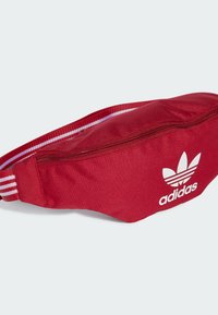 Červená ledvinka z odolné látky, s předním zipem, bílým logem Adidas a pruhovaným nastavitelným popruhem.