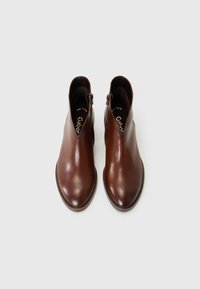 Bottines en cuir marron avec une texture lisse, dotées d'une fermeture éclair sur le côté et d'un design à bout arrondi, posées sur un fond uni.