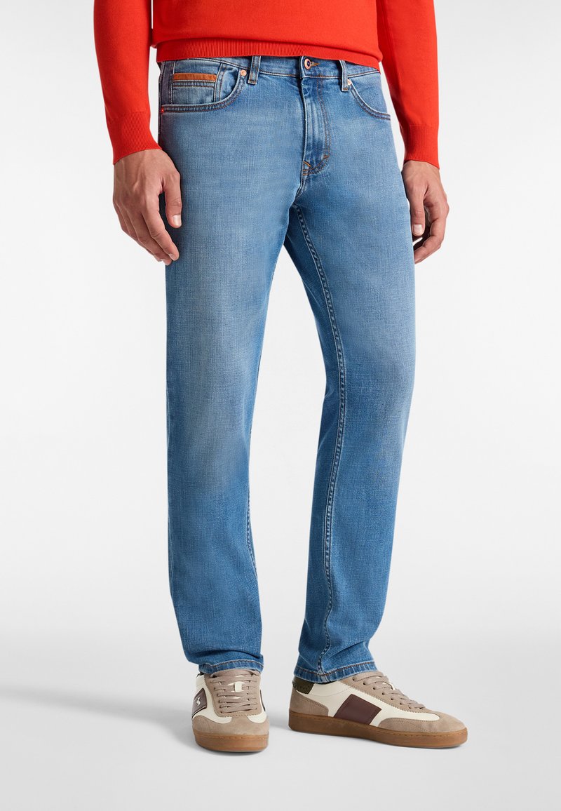 Los jeans azul claro tienen un corte recto, cinco bolsillos y costuras en contraste. Se llevan con zapatillas beige y gris con acentos marrones.