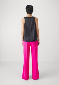 Top senza maniche in satin nero abbinato a pantaloni larghi rosa brillante. L'outfit presenta una vestibilità comoda e dettagli minimi.