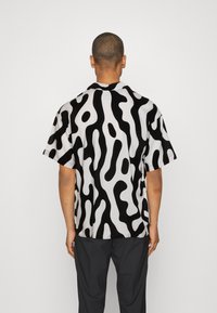 Camicia a maniche corte con un motivo astratto a onde in bianco e nero, realizzata in tessuto leggero con una vestibilità comoda e colletto a risvolto.