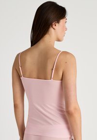 Top rosa con spalline sottili e regolabili, superficie liscia e schiena dritta. Design semplice, adatto per essere indossato a strati.
