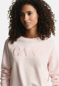 Felpa leggera rosa pallido con logo "GANT" in rilievo dello stesso colore e testo "NEW HAVEN" sottostante. Tessuto morbido con vestibilità rilassata.