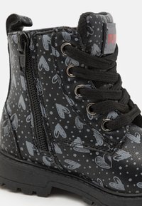 Botte de combat noire avec motif de cœurs gris et de pois, en cuir texturé, à lacets à l'avant et détail de fermeture éclair sur le côté. Semelle en caoutchouc épaisse.