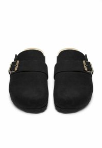 Svarta mockaklogs med en bred rem och en metallspänne, rund tå och strukturerad yta. Sulan är platt och något upphöjd.