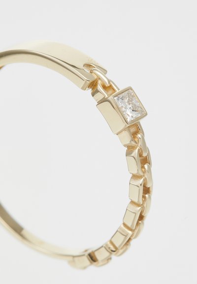 Gold ring with a linked design and a square-cut clear stone set in a smooth gold bezel. Polished surface with shiny texture.