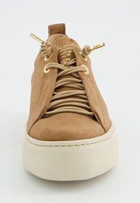 Baskets en daim beige avec un bout arrondi, une semelle en caoutchouc crème et un design à lacets plats. Détails dorés sur les œillets et la languette avec un texte.