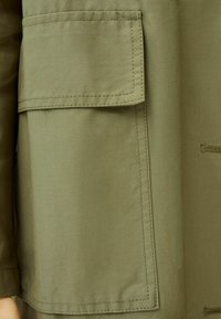 Olive green fabric with a smooth texture; features a large patch pocket on the side, with stitching details along the edges.