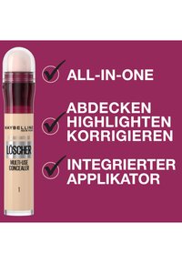 Correcteur multi-usages Maybelline dans un tube transparent avec un capuchon rose ; présente un applicateur intégré et des étiquettes en texte blanc sur un fond violet.