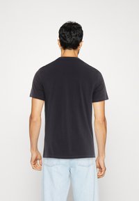 Short-sleeve black t-shirt made of soft cotton, featuring a classic crew neck and a relaxed fit, worn with light blue denim jeans.
