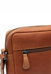 Borsa in pelle marrone con una superficie liscia, bordi arrotondati e chiusura con zip. Presenta una linguetta metallica e dettagli cuciti.