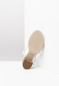 Sandale à talons blancs avec une semelle beige lisse, des sangles ajustables et un branding discret, mettant en avant un design minimaliste et une forme élégante.