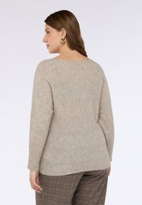 Beżowy sweter na drutach z poziomymi wzorami pasków, z szerokim dekoltem i długimi rękawami, w połączeniu z brązowymi spodniami w kratę.