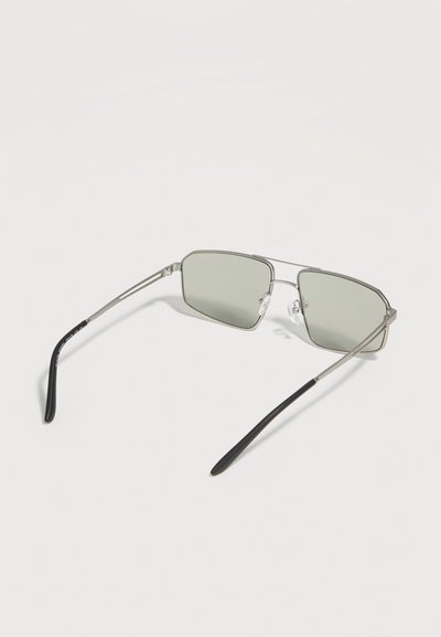Ορθογώνια γυαλιά ηλίου με ασημένιο μεταλλικό σκελετό και φακούς με πράσινη απόχρωση, μαύρες άκρες στα μπράτσα, τοποθετημένα πάνω σε λευκή επιφάνεια.