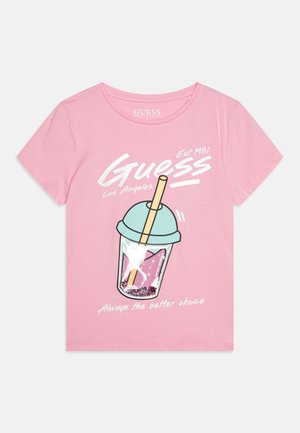 T-shirt rose à manches courtes présentant un graphique d’une tasse avec un couvercle bleu et une paille, avec un texte blanc indiquant "Guess Los Angeles" et "Always the better choice."
