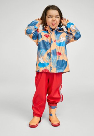 Bunte wasserdichte Regenjacke mit blauen Wolken- und Regenschirmmustern, kombiniert mit leuchtend roten Regenhosen und passenden Stiefeln.