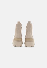 Botas de tobillo beige con parte superior de tela texturizada, cremalleras traseras y suelas de goma gruesa con profundas estrías para mayor tracción.