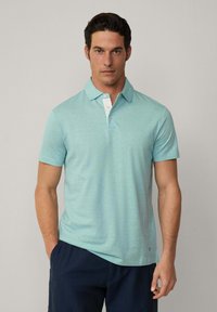 Polo de color azul claro con una textura suave, de manga corta y con una tapeta blanca. El corte es relajado, combinado con pantalones cortos azul marino.