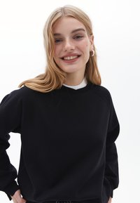 Felpa nera con scollo rotondo, maniche raglan e vestibilità comoda. Presenta una texture morbida e un design minimalista.