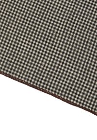 Tessuto a scacchi bianco e nero con un motivo a trama, caratterizzato da una superficie testurizzata e un bordo lavorato all'uncinetto marrone.