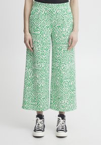 Pantalons larges en vert et blanc avec un motif géométrique complexe. Fabriqués en tissu léger, dotés de poches latérales et d'une ceinture lisse.