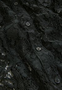 Black lace fabric with intricate floral patterns, featuring a textured surface and black button closures.