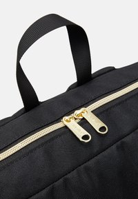 Czarna materiałowa torba z dwoma złotymi suwakami i czarnym plecionym uchwytem do noszenia na górze na białym tle.