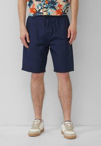 Tummansiniset shortsit, jotka on valmistettu kevyestä kankaasta. Niissä on joustava vyötärönyöri ja sivutaskut. Yhdistä vaaleanbeigeihin sneakers-kenkiin.
