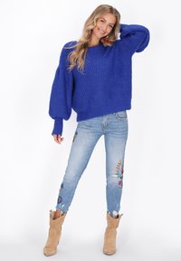 Maglione azzurro lavorato a maglia con maniche a palloncino, abbinato a jeans chiari strappati con ricami floreali. Stivaletti color camoscio con ritagli.