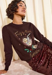 Maglione marrone con una grafica di una bevanda festiva arricchita da paillettes, abbinato a una gonna scintillante color borgogna in paillettes. Materiale in maglia morbida e testurizzata.