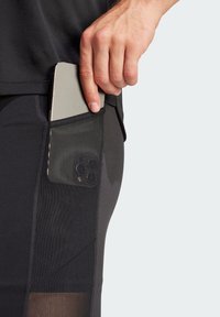 Czarne spodenki sportowe z boczną kieszenią na smartfon, z siatkowym panelami dla lepszej widoczności i eleganckim, dopasowanym krojem.