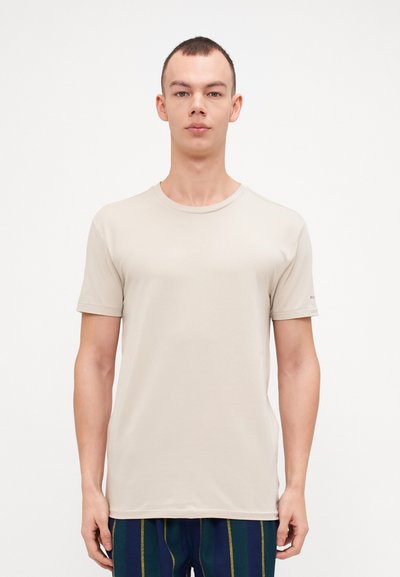 T-shirt beige à manches courtes en tissu doux, avec un col rond et des détails de couture subtils. Porté avec un pantalon rayé bleu.