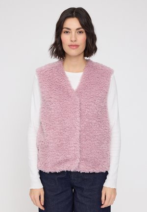 Rosa, flauschige Weste mit einer weichen, strukturierten Oberfläche, mit V-Ausschnitt und offener Vorderseite. Über einem weißen Langarmshirt getragen.