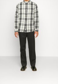 Svart och vit rutigt knäppskjorta med långa ärmar, kombinerad med mörka byxor och svarta skor. Slät tyg med en strukturerad passform.