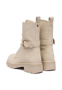 Beżowe skórzane botki za kostkę o teksturowanym wykończeniu, z boku z klamrą, z tyłu z uchwytem do zakładania oraz masywną, jasnobrązową gumową podeszwą.