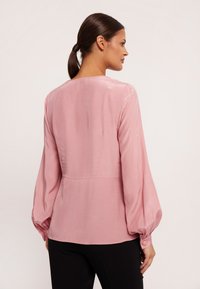 Różowa satynowa bluzka o luźnym kroju, z długimi bufiastymi rękawami, okrągłym dekoltem i zapięciem na guziki, charakteryzująca się gładką, lekką teksturą.