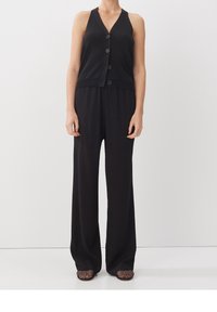 Czarny kombinezon z dekoltem w serek, sześcioma guzikami i szerokimi nogawkami. Wykonany z gładkiego materiału o luźnym kroju. Noszony z codziennym obuwiem.