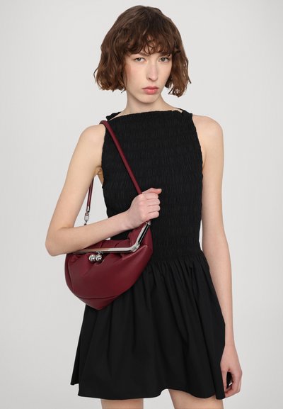 Red synthetic handbag with a rounded shape, silver hardware, and two decorative metal balls. Worn with a black smocked sleeveless dress.