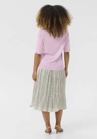 Gaiši rozā adīta blūze ar īsām piedurknēm kombinēta ar plisētu, sudrabpelēku midi svārku, kas ir ar teksturētu rakstu. Vienkārši brūni sandales.