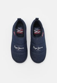 Zapatillas oscuras de lona con diseño en denim, que presentan un diseño acolchado, bordado blanco del logo y una etiqueta de tela con la bandera del Reino Unido.