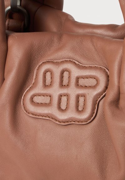 Κοντινή λήψη καφέ δερμάτινης τσάντας με ραμμένη επένδυση που διαθέτει κάθετες και οριζόντιες ορθογώνιες περικοπές.