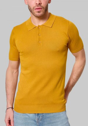 Polo shirt jaune moutarde à manches courtes en tissu tricoté doux, avec un col, une patte de boutonnage à quatre boutons et des bords côtes aux manches et à l'ourlet.