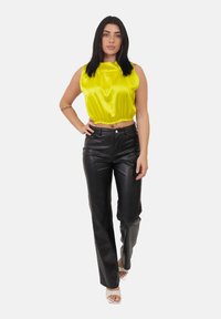 Top corto in satin giallo brillante con orlo elasticizzato, abbinato a pantaloni svasati in pelle nera. Il modello indossa sandali bianchi con tacco e punta aperta.
