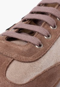 Acercamiento de una zapatilla de ante marrón con cordones de tela a juego pasados por ojales de metal.