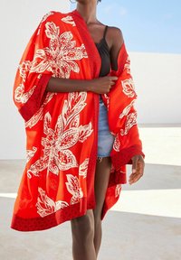 Kimono rouge à motifs floraux en tissu léger, présentant un large drapé, une bordure rouge et des motifs blancs complexes sur toute la surface.