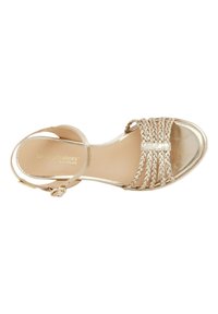Sandal in metallo dorato con cinturini intrecciati, punta chiusa e cinturino alla caviglia. Texture liscia con una fibbia sul lato.